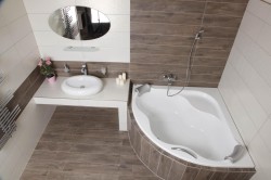 Rohová vana s obložením v dekoru dřeva, bílé obklady a umyvadlový pult s oválným zrcadlem; pohled shora na vanovou zónu