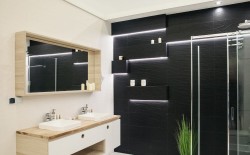 Černá akcentní stěna se zapuštěnými policemi a LED linkami, vedle sprchový kout; umyvadla pod zrcadlovou skříňkou
