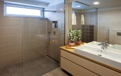 Koupelna s prostorným sprchovým koutem a širokým umyvadlem, závěsná svítidla nad deskou a velké zrcadlo odrážející světlo do místnosti