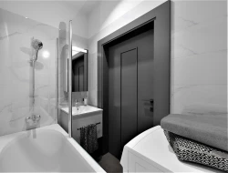 Paneláková koupelna s vanou a umyvadlem; bílé mramorové obklady a kontrastní tmavé dveře