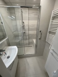 Úzká světlá koupelna se sprchovým koutem s posuvnými dveřmi, žebříkovým radiátorem a malým umyvadlem na skříňce