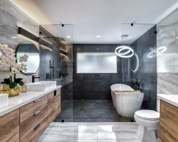 Prostorná koupelna s vanou i sprchou oddělenou sklem, dřevěnými skříňkami pod umyvadlem, kruhovým závěsným světlem a velkým oknem s matným sklem.