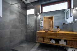 Šedá koupelna s velkou sprchou se skleněnou zástěnou, masivní dřevěnou umyvadlovou deskou s miskovým umyvadlem a úložnými koši ve spodní polici