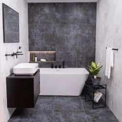 Kombinace vany a umyvadla: bílá vana s černou baterií, tmavý šedý obklad s osvětlenou nikou na kosmetiku a závěsná skříňka s umyvadlem