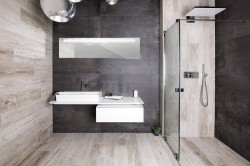 Moderní koupelna s kombinací šedých obkladů a dekoru světlého dřeva, závěsnou skříňkou s umyvadlem a čirým sprchovým koutem s horní sprchou