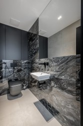 Moderní toaleta s kompaktním umyvadlem, kontrast světlé podlahy a tmavého kamenného obkladu