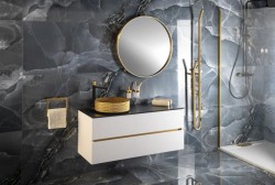 Bílá závěsná skříňka s černou deskou, kulaté zrcadlo se zlatým rámem a walk-in sprcha se zlatými profily na tmavém obkladu