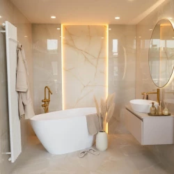 Volně stojící vana v béžové koupelně, zlatá stojánková baterie a podsvícený mramorový panel jako dominantní prvek stěny