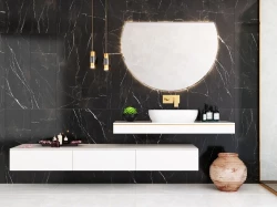 Luxusní umyvadlová zóna na černém mramoru: bílé deskové umyvadlo, zlatá baterie, velké půlkruhové podsvícené zrcadlo a závěsná světla