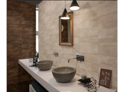 Dvojice kamenných miskových umyvadel na bílé desce, nástěnné baterie a dřevěný rám zrcadla v teplém hnědobéžovém ladění