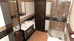 Koupelna s rohovým sprchovým koutem, bílým umyvadlem na skříňce a vodorovnými pruhy obkladů v bílé, béžové a tmavě hnědé