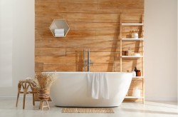 Volně stojící vana před dřevěným obkladem, dřevěná otevřená police na kosmetiku, světlá dlažba