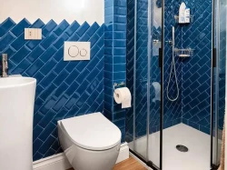 Malá koupelna s modrým obkladem ve vzoru rybí kosti, závěsným WC a sprchovým koutem s černými profily a posuvnými dveřmi