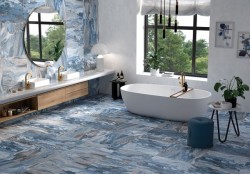 Prostorná koupelna s modrobílým mramorovým dekorem na stěnách i podlaze, volně stojící vanou, dvojitým umyvadlem a zlatými bateriemi