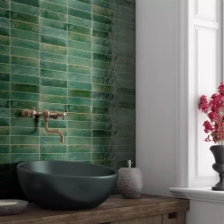 Detail umyvadla: tmavé miskové umyvadlo na dřevěné desce, zelené „cihličkové“ obklady a nástěnná baterie v retro stylu