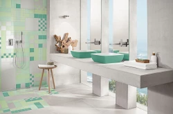 Světlá koupelna s mozaikou v zelených tónech, dvěma tyrkysovými umyvadly na betonové desce a sprchou s podomítkovou baterií