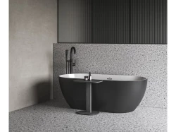 Matně černá volně stojící vana na terrazzo podlaze, černá stojánková baterie a šedé stěny v minimalistickém provedení