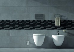 Detail závěsného WC a bidetu na šedých obkladech s černým mozaikovým pruhem a doplňky v chromu