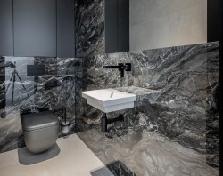 Malá černošedá toaleta s výrazným mramorovým dekorem, závěsným umyvadlem, černou podomítkovou baterií a WC v tmavém provedení