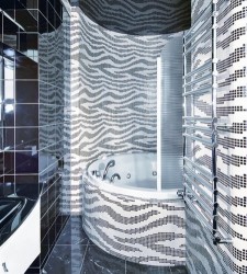 Šedobílá koupelna s výraznou „zebra“ mozaikou na stěnách a obezděnou rohovou vanou; chromový žebříkový radiátor v popředí