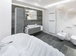 Elegantní koupelna s šedým obkladem v dekoru dřeva, umyvadlem na skříňce, podsvíceným zrcadlem a závěsným wc a bidetem