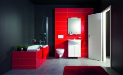 Kontrastní koupelna s tmavými stěnami, červeným obkladem vany a stěny za umyvadlem; závěsné WC