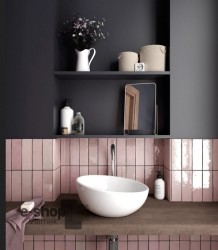 Detail umyvadlového koutku: bílé asymetrické umyvadlo na dřevěné desce, lesklé růžové obklady „cihličky“ a otevřené police s doplňky