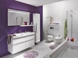 Bílo-fialová koupelna s umyvadlovou skříňkou, velkým zrcadlem, závěsným WC a bidetem; fialová akcentní stěna a kulaté koupelnové předložky