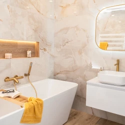 Koupelna s vestavnou vanou, nikou s podsvícením a dřevodekorem, zlatou vanovou baterií a bílým umyvadlem na závěsné skříňce