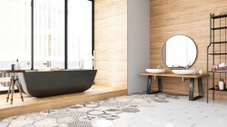 Interiér s volně stojící tmavou vanou na dřevěné podestě, umyvadly na dlouhé dřevěné lavici, kulatým zrcadlem a patchworkovou dlažbou