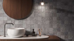 Detail umyvadlové zóny: bílé umyvadlo na desce, velké kruhové zrcadlo a mozaikový obklad v šedém kamenném vzhledu