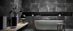 Tmavá koupelna s velkoformátovým betonovým obkladem, bílou volně stojící vanou a minimalistickými doplňky v černé barvě