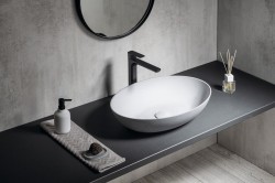 Detail umyvadlové zóny s oválným bílým umyvadlem, černou baterií a stěrkou v jemném betonovém dekoru