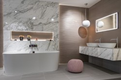 Elegantní koupelna s bílým mramorovým obkladem, dvěma umyvadly na desce, volně stojící vanou a jemně růžovým taburetem