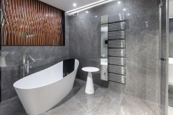 Šedá koupelna s mramorovým dekorem, volně stojící minimalistickou vanou, vysokým chromovým radiátorem a dekorativní panely na stěně