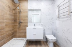 Světlá klasická koupelna s bílým nábytkem, sprchovým koutem v dřevodekoru a chromovaným koupelnovým žebříkem na mramorovém obkladu